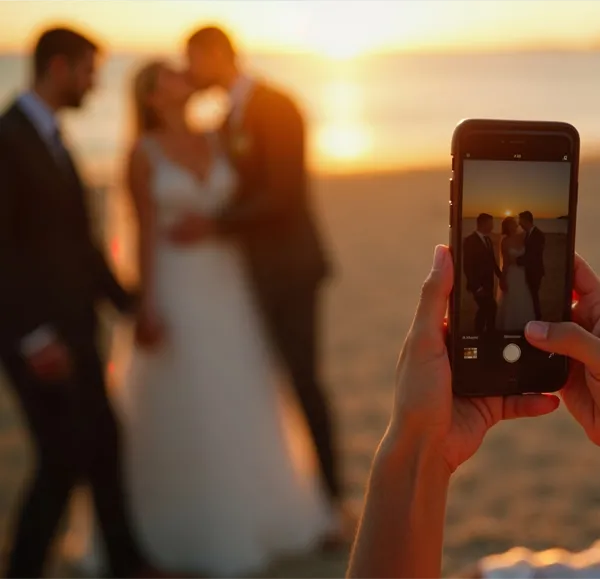 Hochzeitspaar am Meer, das von einem Gast Fotografiert wird.